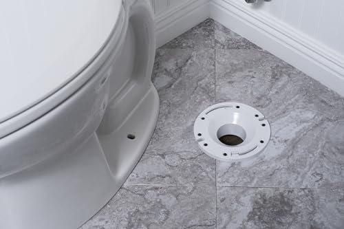 White PVC closet flange with plastic ring mounted on gray tile floor next to white toilet base.