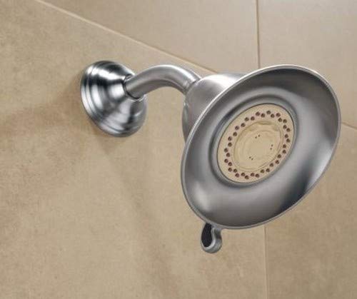 Stainless steel shower head with curved arm mount and circular spray face mounted on beige tile wall.