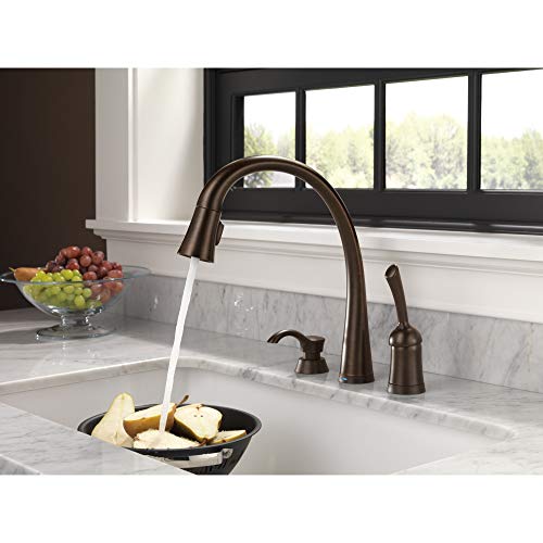 Chrome soap and lotion dispenser with pump mechanism mounted on kitchen sink countertop.