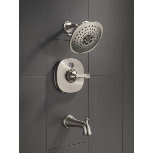 Polished brass shower arm with round showerhead, valve trim, and tub spout mounted on gray tile wall.