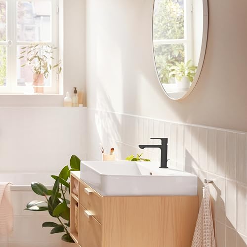 Matte black single-hole bathroom faucet with tall spout installed on white rectangular sink above wooden vanity.