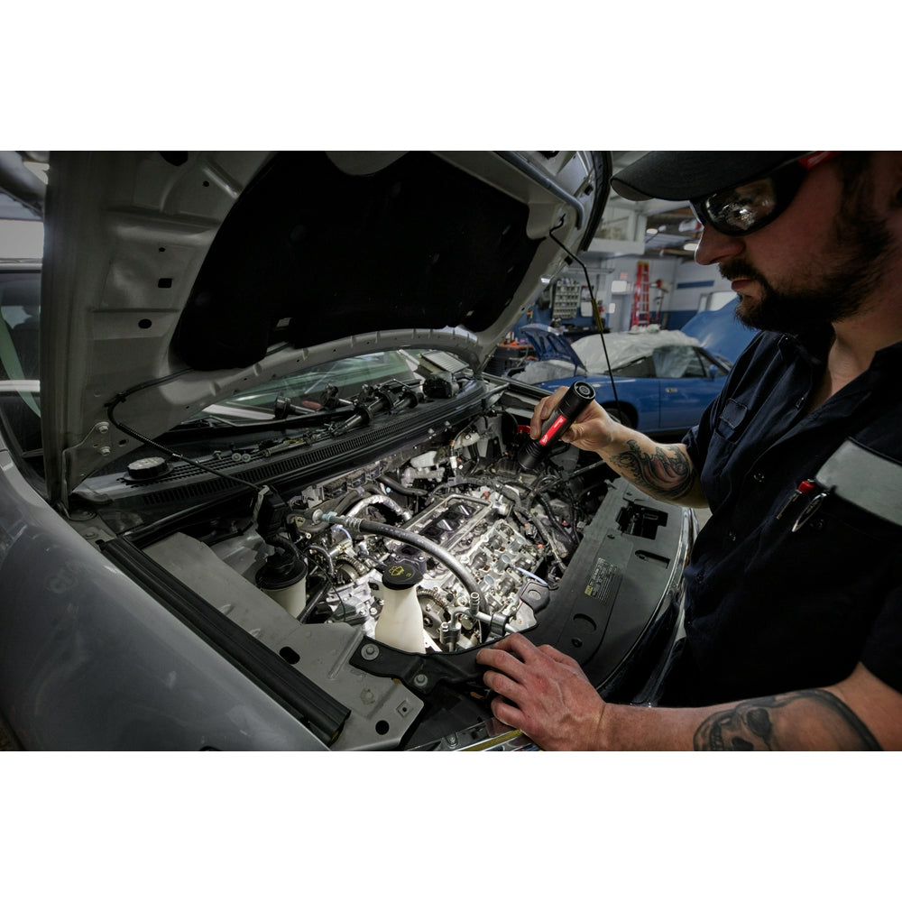 Mechanic holding red flashlight while inspecting car engine under open hood.