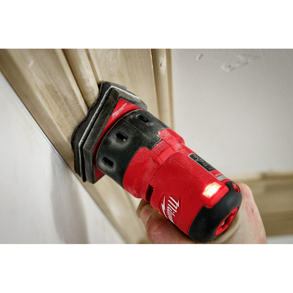 Black sponge interface pad attached to red and black Milwaukee orbital detail sander being held against wood surface.