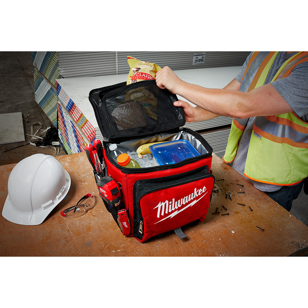 Red Milwaukee cooler with black interior compartments, open to display mesh pocket and storage sections on jobsite.