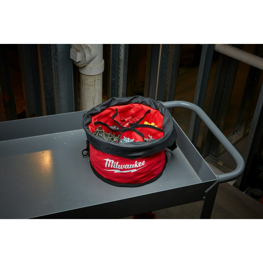 Red and black cylindrical organizer bag with Milwaukee branding and black straps sitting on a metal surface.