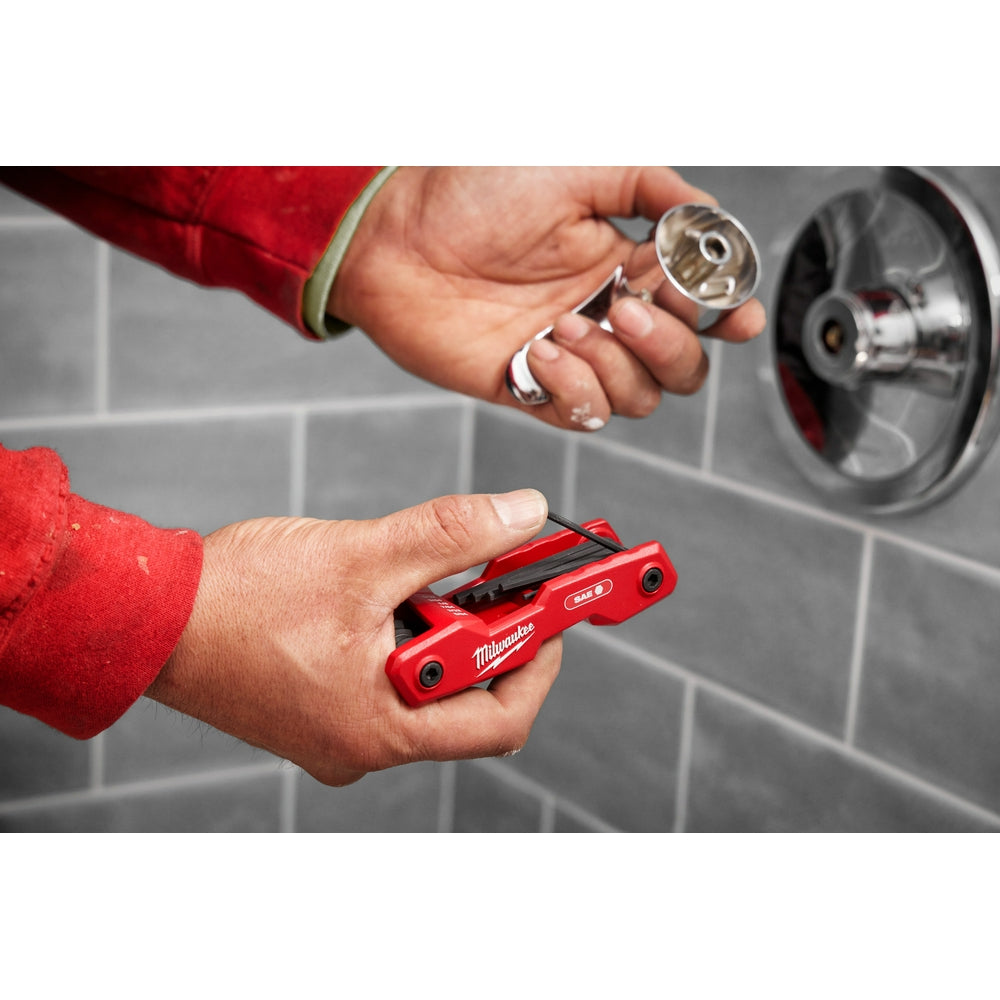 Red Milwaukee folding hex key set with nine SAE keys displayed open in hand near a vehicle wheel.