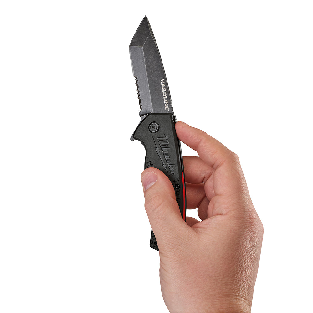 Black steel folding pocket knife with serrated blade held open in hand, showing black handle with red accent and Milwaukee br