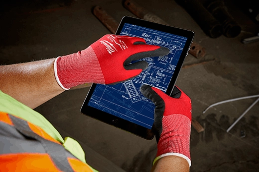 Red nitrile-dipped work gloves with white cuffs worn while operating a touchscreen tablet.