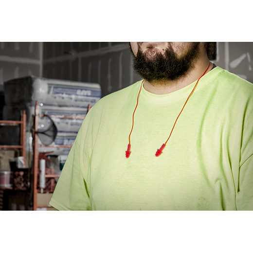Red corded ear plugs with connecting cord worn around neck in workshop setting.