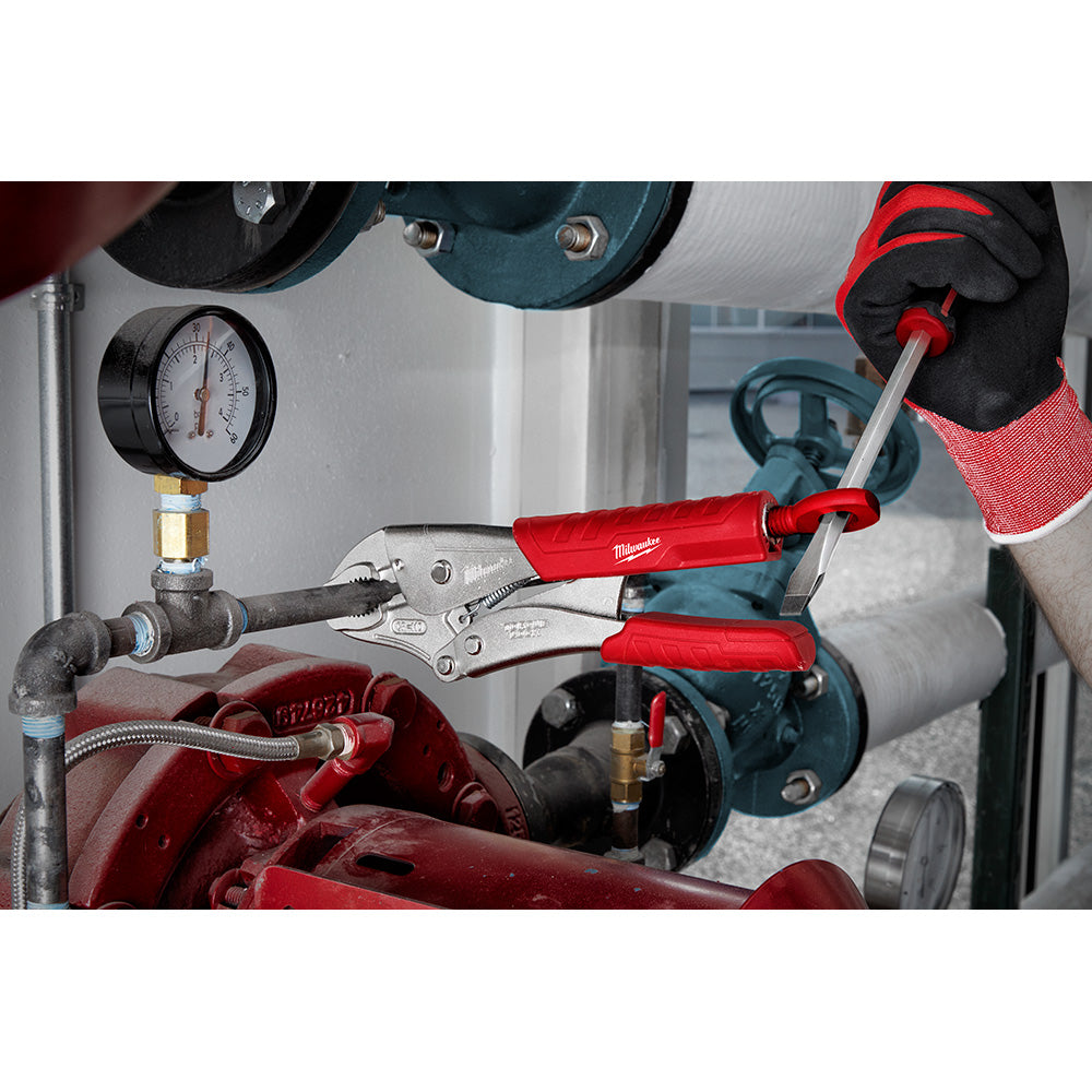 Milwaukee curved jaw locking pliers with red handles being used to grip a pipe in an industrial setting.