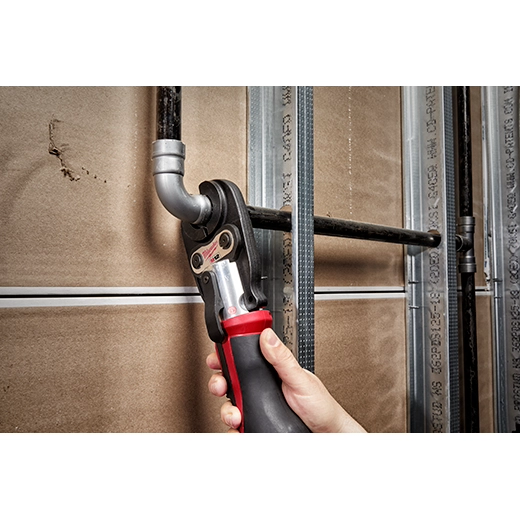 Hand wrapping detectable tape around a metal gas line pipe against a wooden wall background.