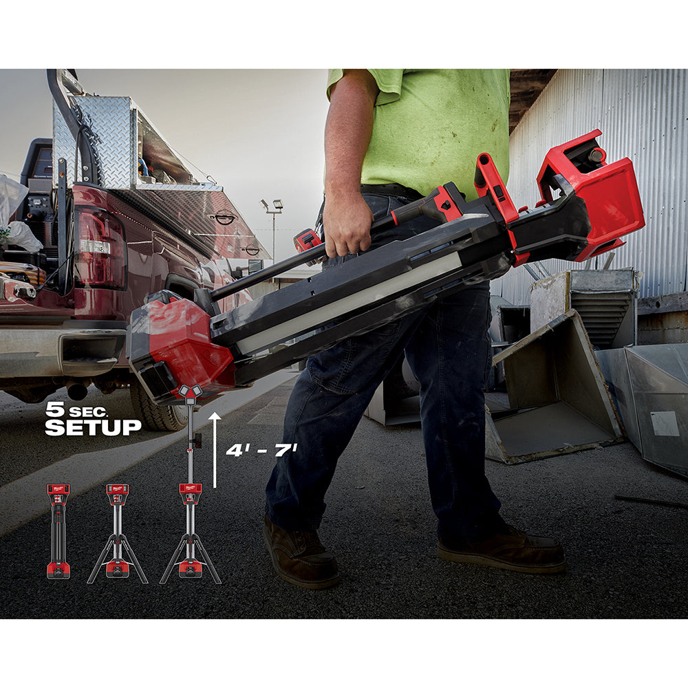 Red and black Milwaukee M18 ROCKET tower light with extending legs held by worker, adjustable 4'-7' height.