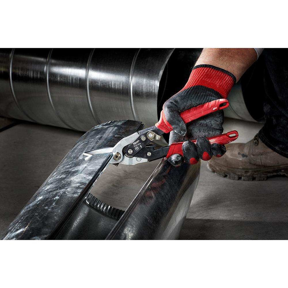 Red and black aviation snips with curved blades cutting through sheet metal held in a gloved hand.