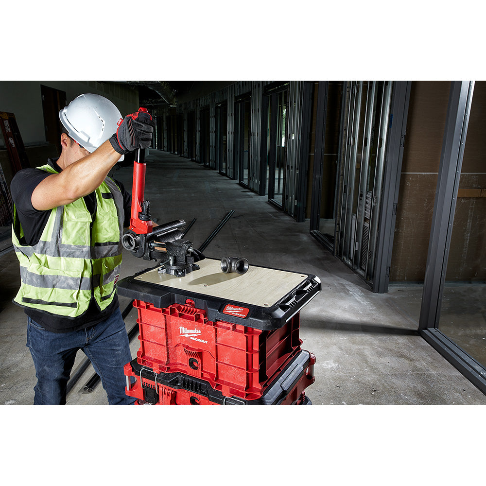 Black work surface mounted on red Milwaukee PACKOUT storage unit with worker using tools on top.