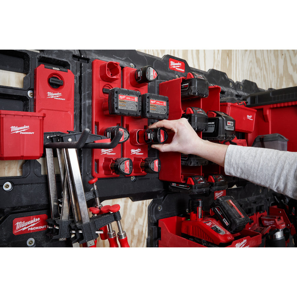 Milwaukee PACKOUT wall-mounted battery rack with red and black storage holding multiple M12 batteries and accessories.