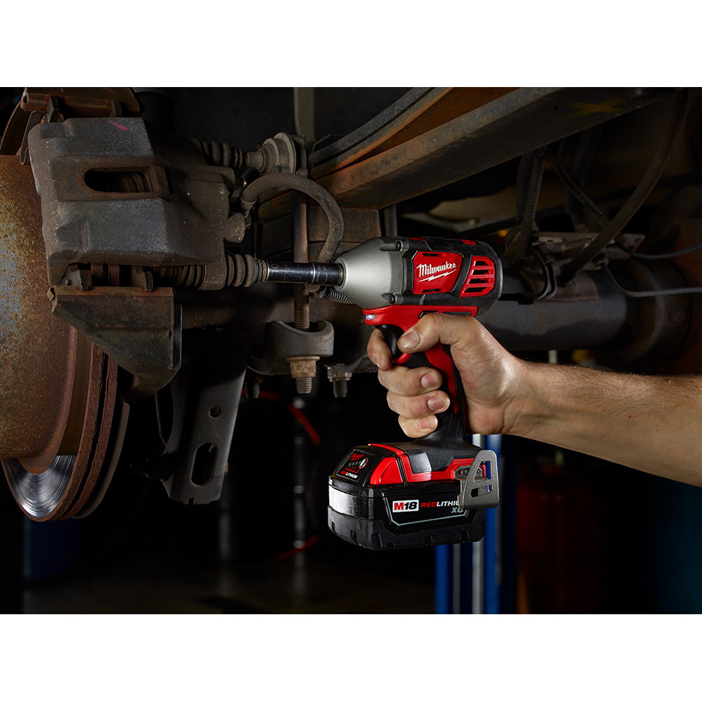 Red and black Milwaukee M18 impact wrench being used on a vehicle brake assembly, with battery visible below.