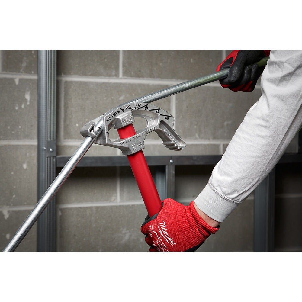 Milwaukee aluminum conduit bender with red handle and shoe, held by worker in red gloves against brick background.