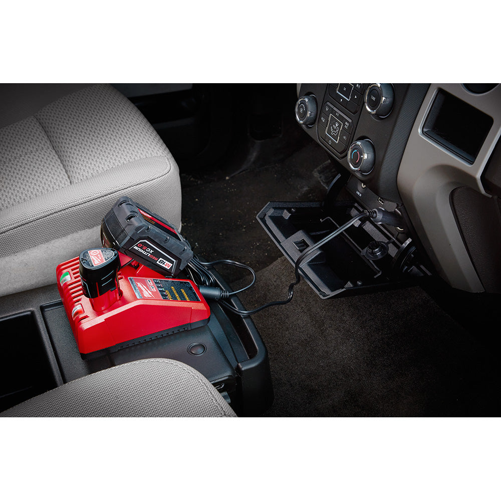 Red and black Milwaukee DC charger with cord mounted on vehicle center console between front seats.