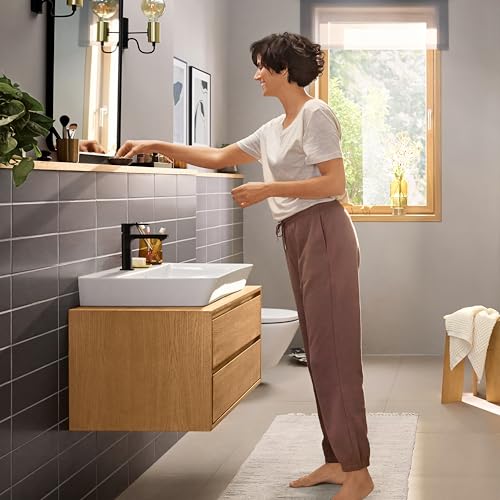 Matte black single-hole bathroom faucet with tall spout installed above white vessel sink on wooden vanity.