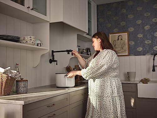 Matte black wall-mounted pot filler faucet with swing arm extended over kitchen counter and pot.
