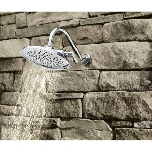 Brushed nickel showerhead with oval face mounted on stone wall, water streaming downward.