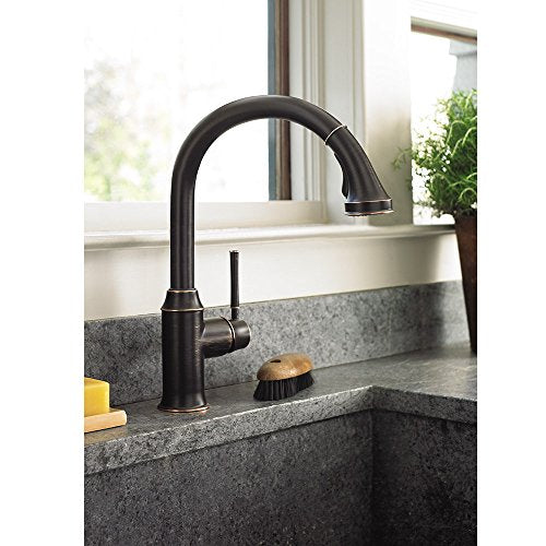 Polished nickel kitchen faucet with arched spout and pull-down spray head mounted on gray countertop.