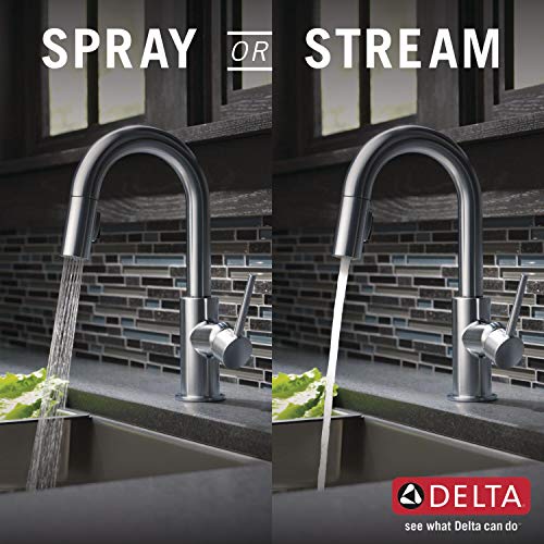 Chrome pull-down bar faucet with dual spray and stream modes over sink with brick backsplash.