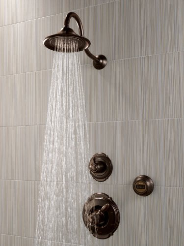 Venetian bronze shower head with wall-mounted controls and water spray stream against vertical tile background.