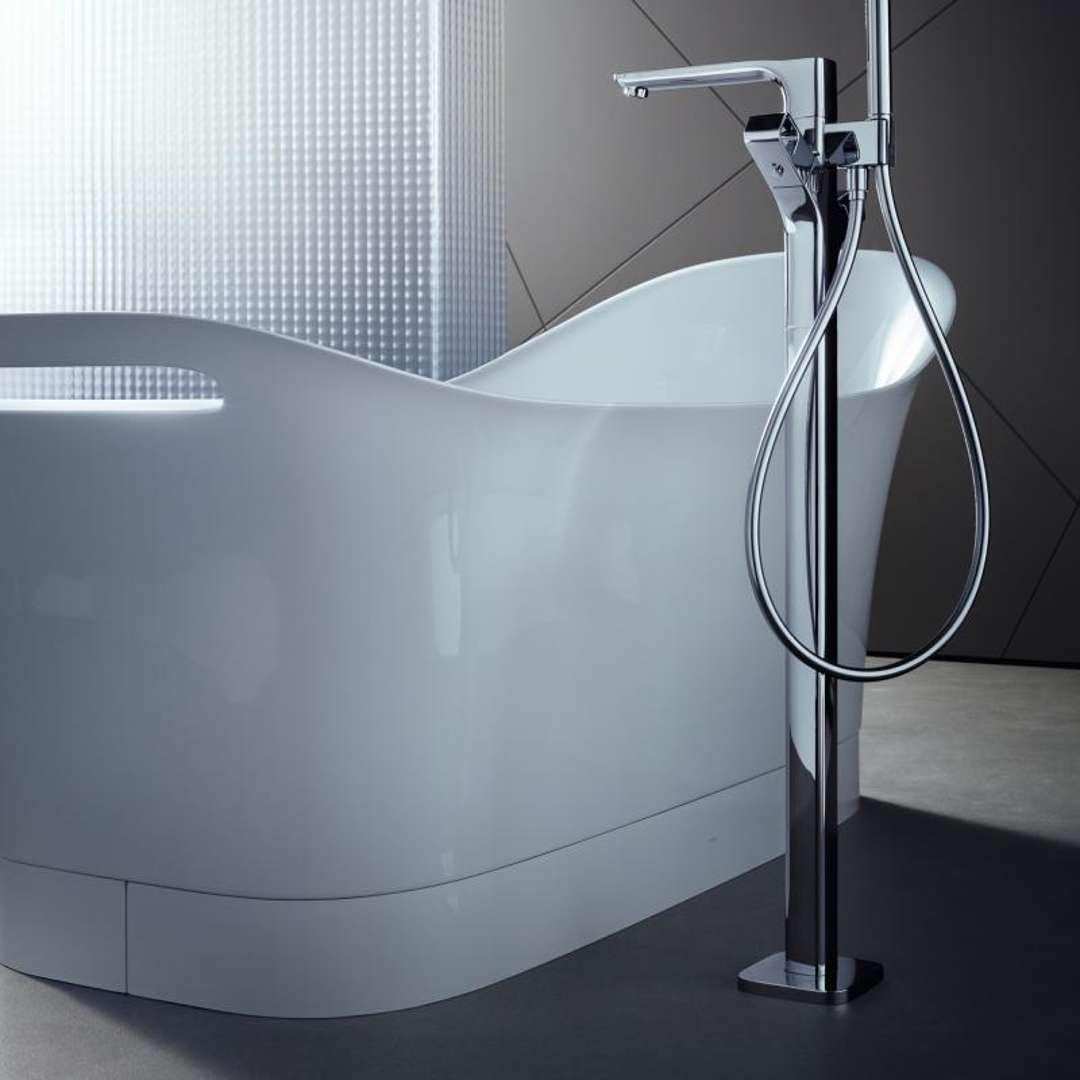 White freestanding bathtub with curved sides and chrome floor-mounted faucet with handheld showerhead.