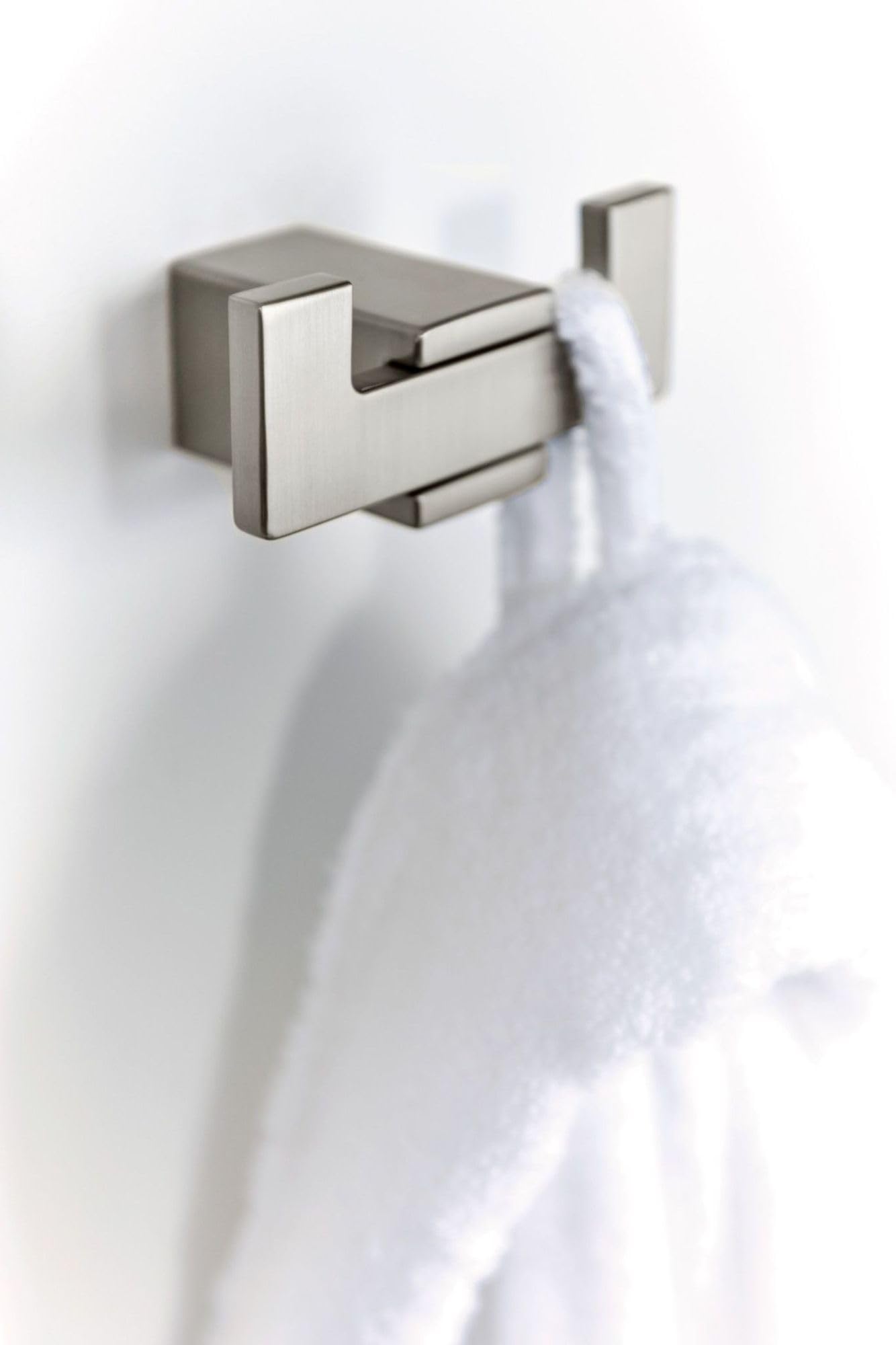 Brushed nickel double robe hook mounted on white wall with white towel hanging from one hook.
