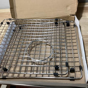 Stainless steel sink grid with square wire pattern and circular drain opening in cardboard box.