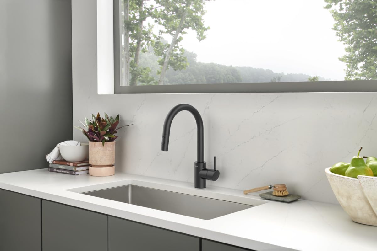 Matte black single-handle pull-down kitchen faucet with curved spout installed above stainless steel sink.