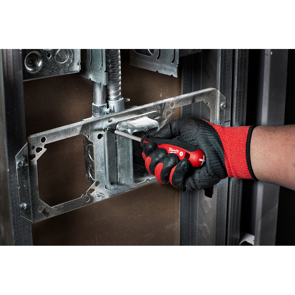 Hand in work glove holding red Milwaukee screwdriver with black grip near metal electrical box.