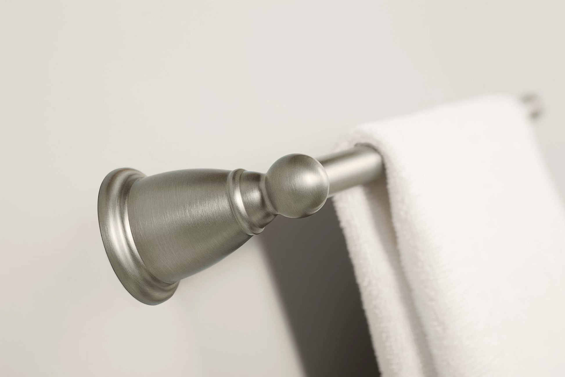 Brushed nickel wall-mounted towel bar with decorative finial and white towel hanging on right side.