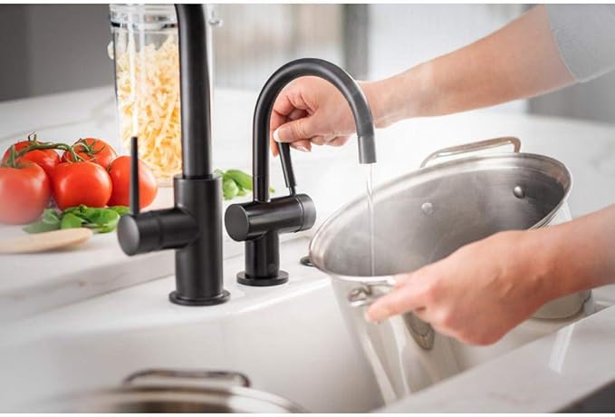 Matte black instant hot water dispenser faucet with curved spout dispensing water into a metal pot on kitchen countertop.