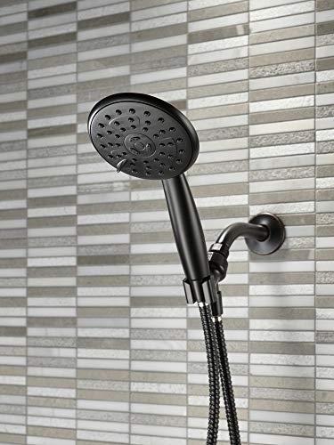 Oil rubbed bronze hand shower with circular perforated face and flexible hose mounted on gray tile wall.