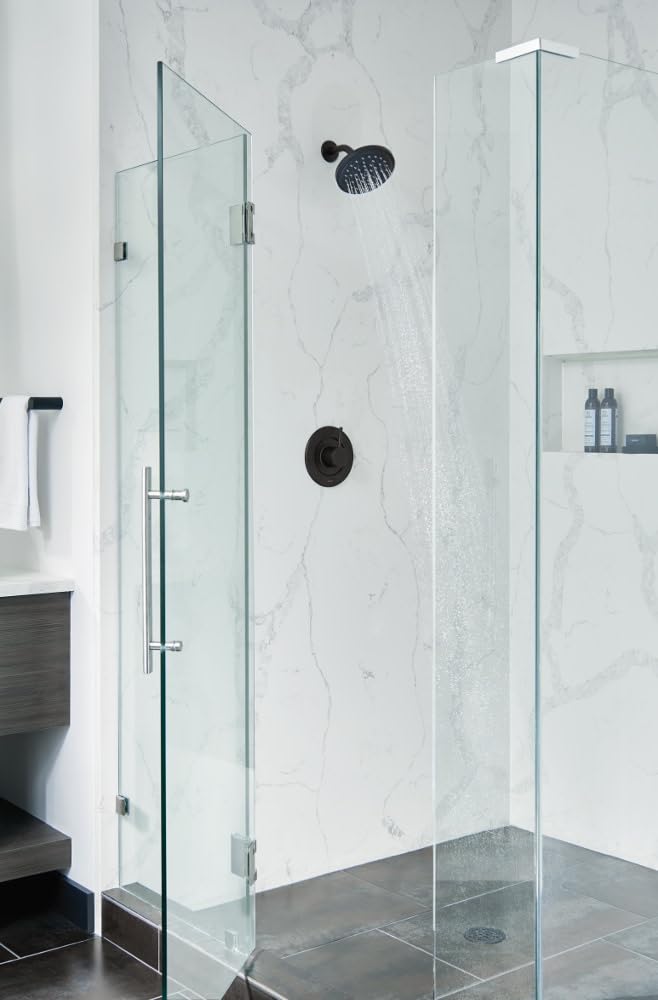 Round black shower head mounted on marble shower wall with control valve below it.