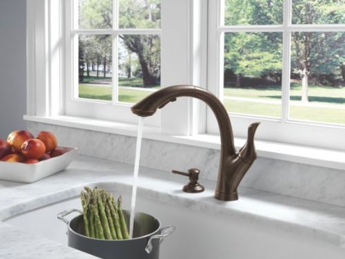 Venetian bronze kitchen faucet with curved spout and single lever handle over sink.