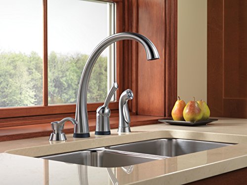 Stainless steel kitchen faucet with curved spout, side sprayer, and soap dispenser pump on countertop.