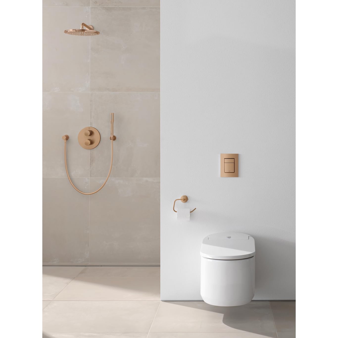 Grohe Essentials brushed gold paper holder mounted on white bathroom wall above toilet.