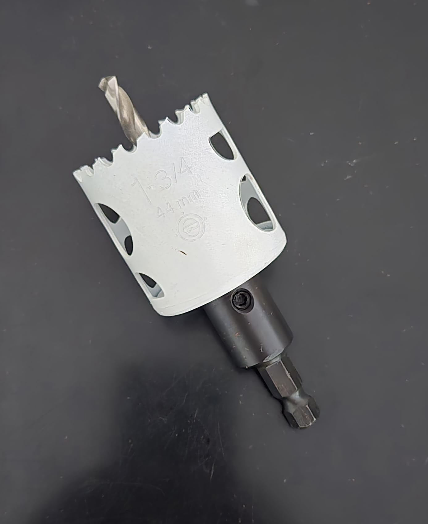White and black bi-metal hole saw with arbor attached, marked 1-3/4" and 44mm, featuring serrated cutting edges and mounting 