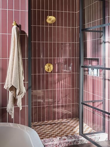Brushed gold shower trim with wide showerhead and lever handle mounted on burgundy tiled shower wall.