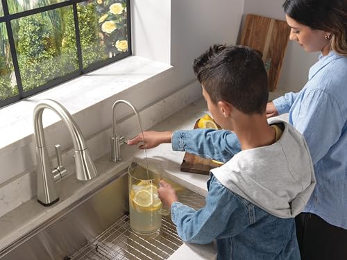 Stainless steel pull-down beverage faucet with curved spout installed above kitchen sink with child and adult using it.