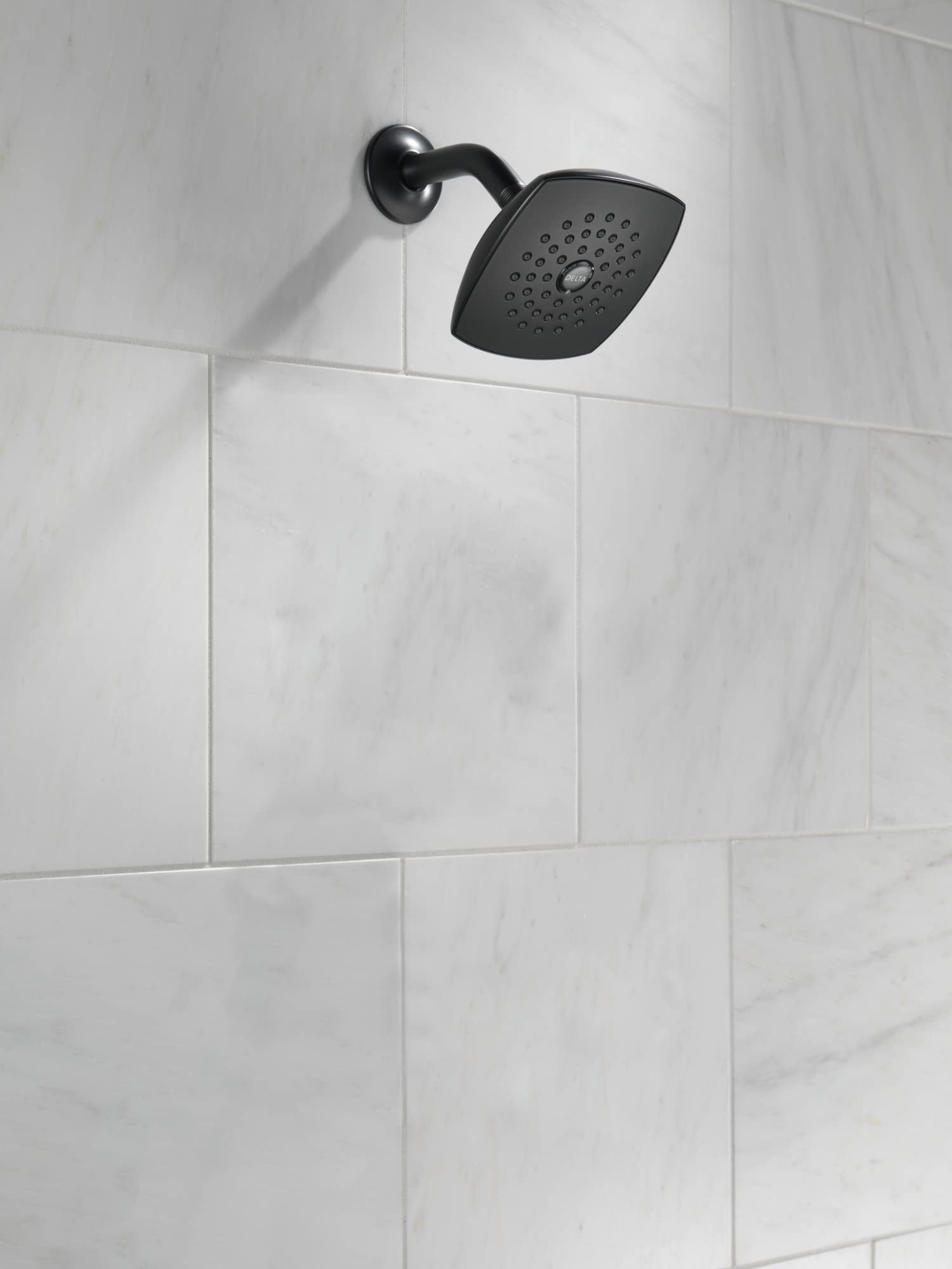 Matte black curved shower arm with square showerhead mounted on white tile wall.