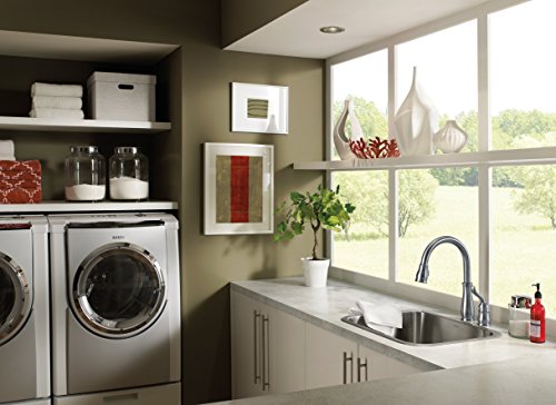 Chrome single-handle pull-down kitchen faucet with soap dispenser mounted above stainless steel sink.