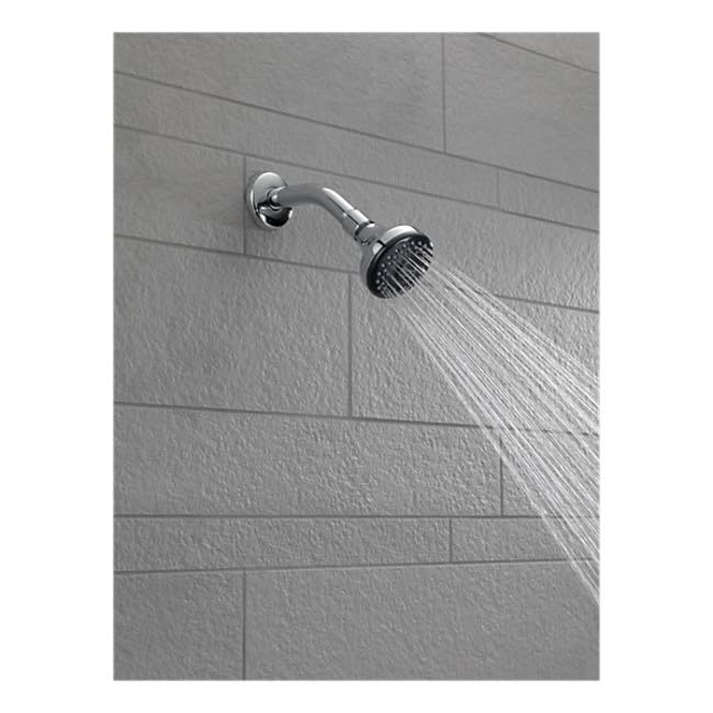 Chrome shower arm with circular showerhead and flange mounted on tile wall, water flowing downward.