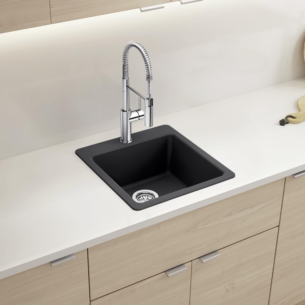 Coal black single bowl kitchen sink with chrome pull-down faucet mounted in white countertop above wood cabinetry.