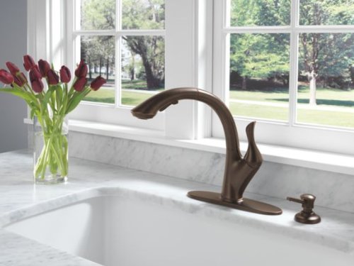 Venetian bronze soap dispenser with curved spout mounted next to kitchen sink faucet.