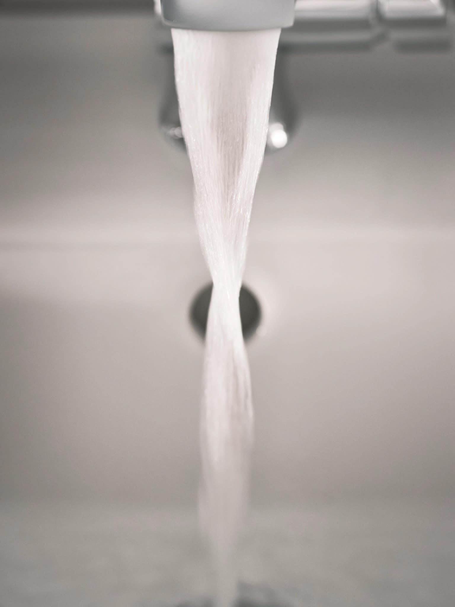 Chrome bathroom faucet with single handle and tapered spout dispensing water stream.