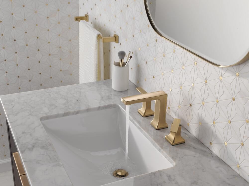 Champagne bronze two-handle widespread bathroom faucet installed on marble countertop with white sink.